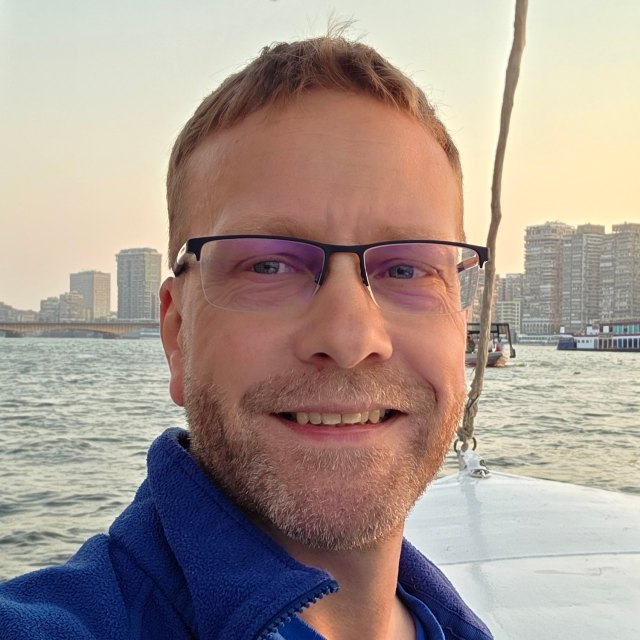 Patrick Fratzscher lächelt an Deck eines Boots in die Kamera, dahinter Wasser im Abendlicht.